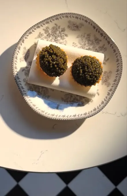 Two caviar tartlets on a floral porcelain plate, lit by hard afternoon sun
