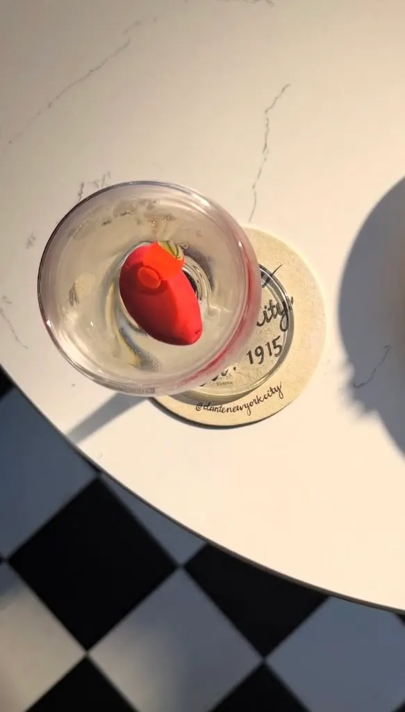 A martini garnished with a red pepper on a marble café table above a checkerboard floor