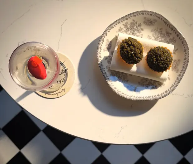 A martini and two caviar tartlets on a marble café table above a checkerboard floor