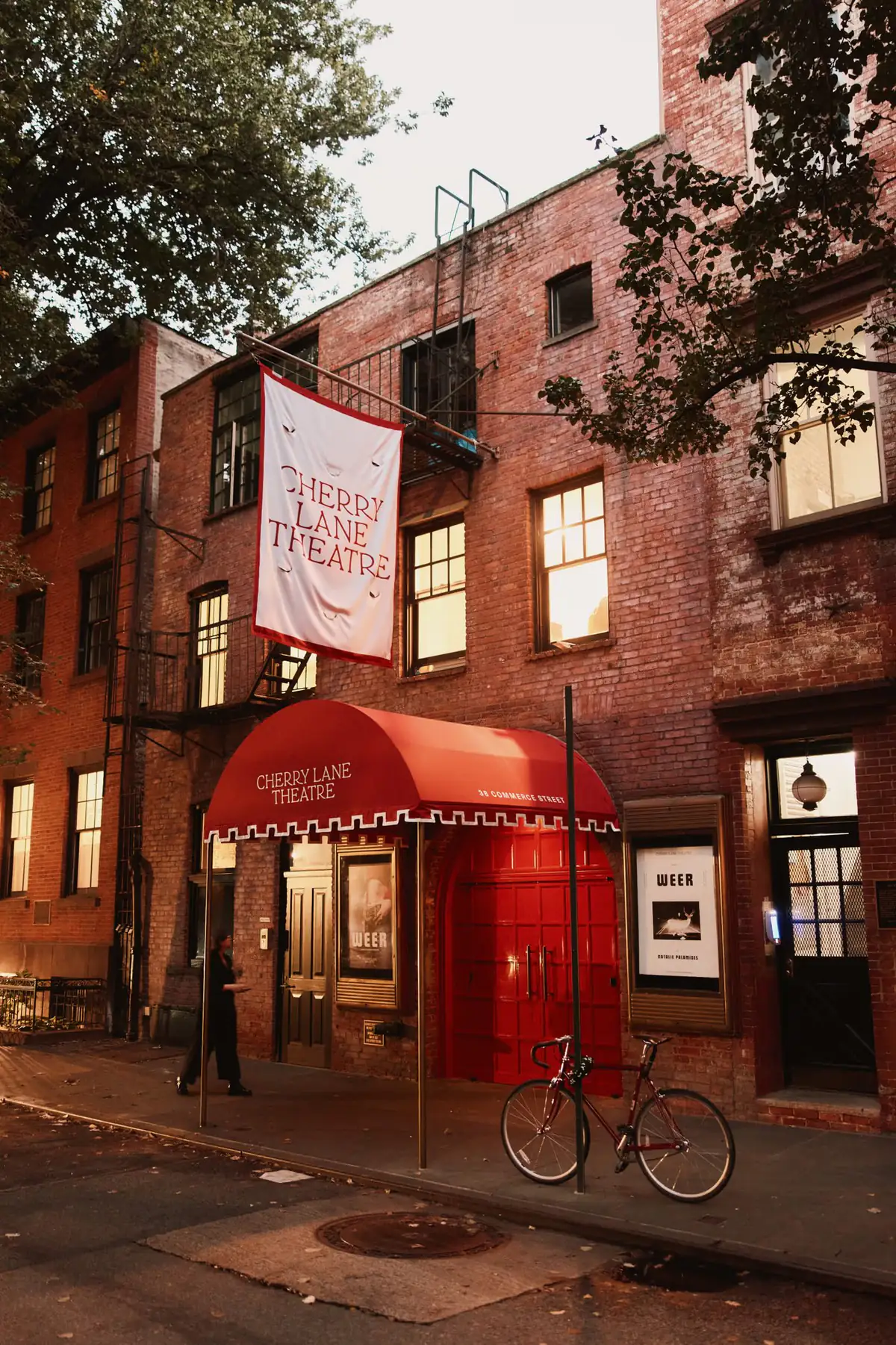 The red brick facade of Cherry Lane Theatre on Commerce Street, its banner and awning lit at dusk